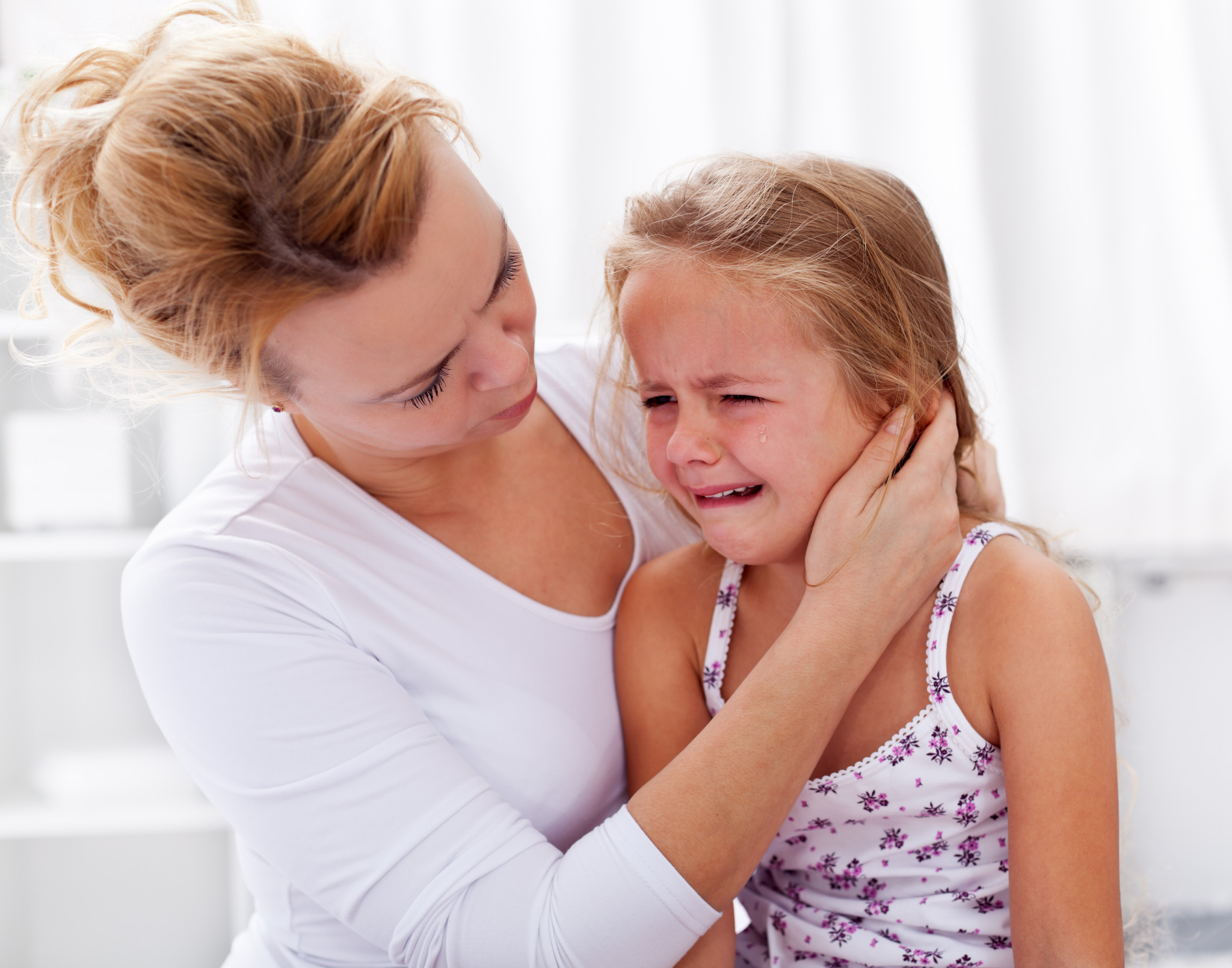 Mother comforting her crying little girl - parenthood concept